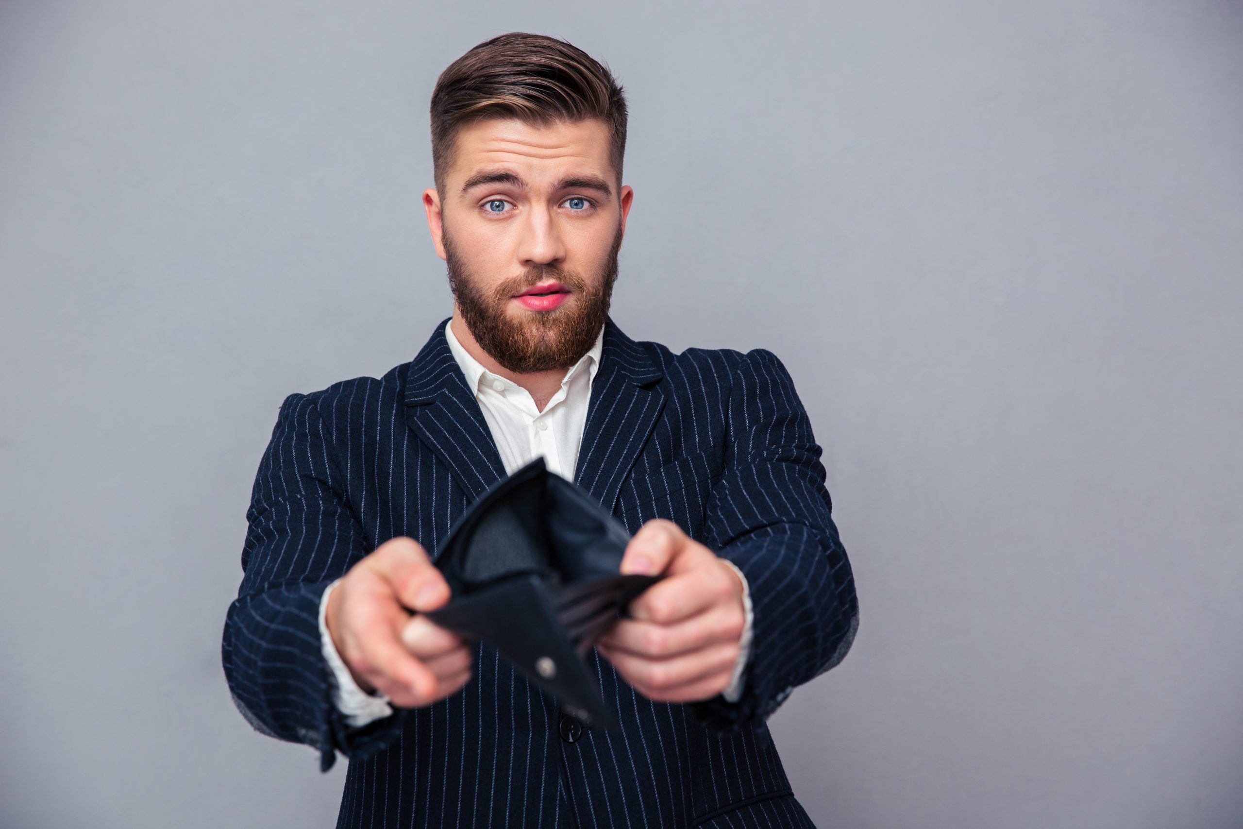 Portrait of a handsome businessman showing his empty wallet over gray background