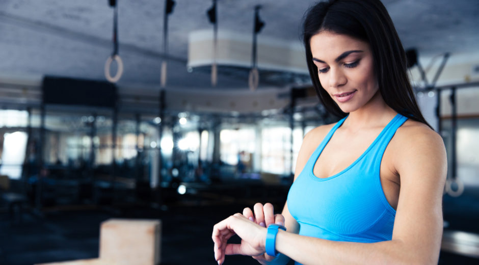 Happy young woman using activity tracker in fitness gym